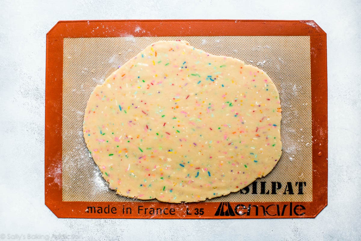 rainbow sprinkle cookie dough rolled out on a silpat baking mat