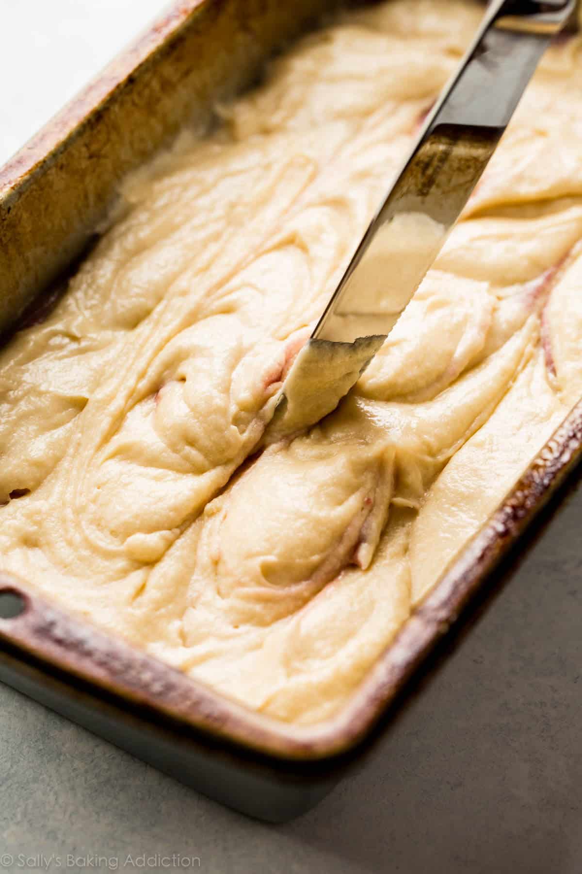pound cake batter in a loaf pan with a knife to swirl the batter around