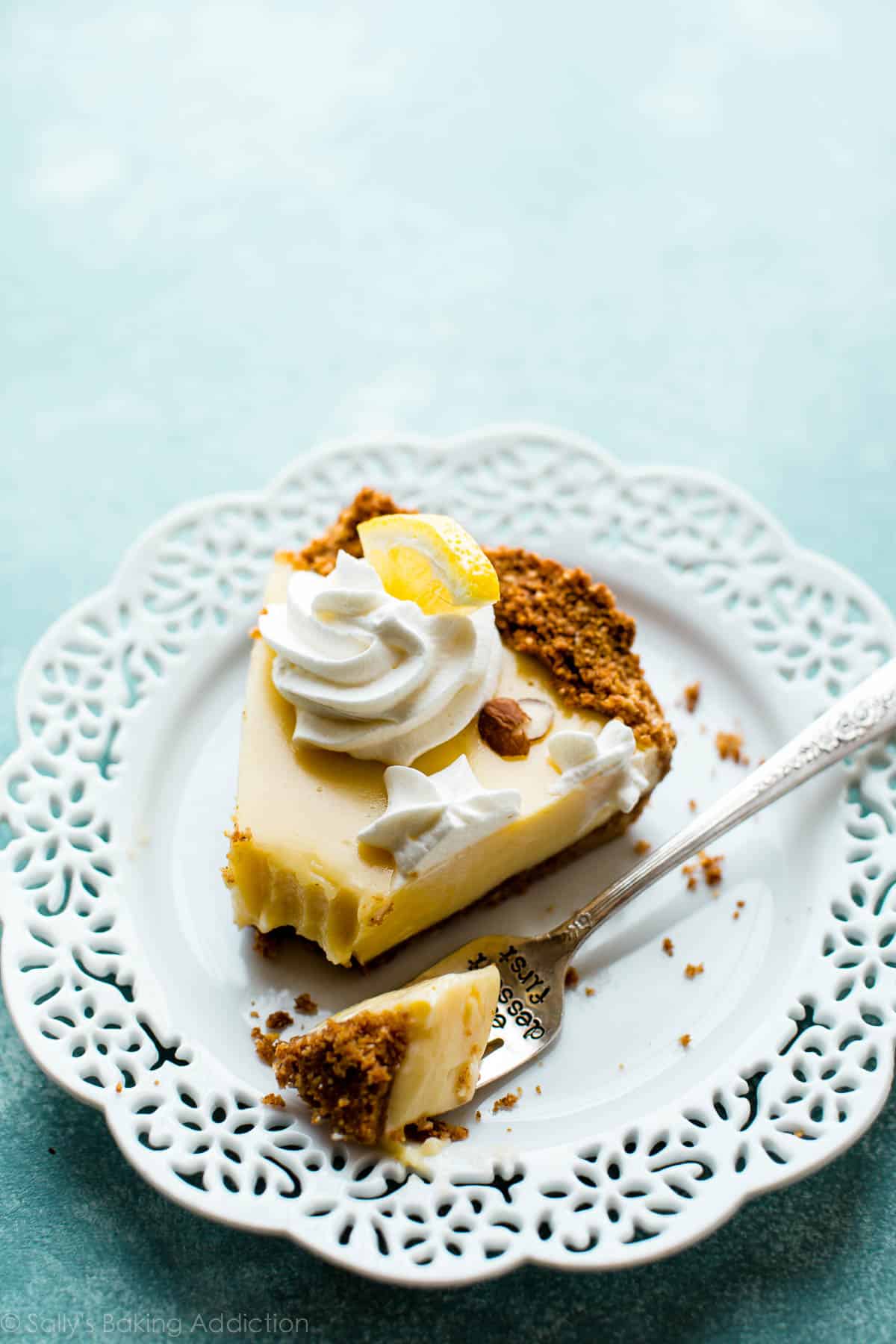 slice of lemon pie topped with whipped cream on a white plate with a fork