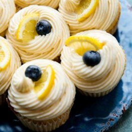 cupcakes with lemon buttercream frosting topped with blueberries and lemon slices on a blue plate