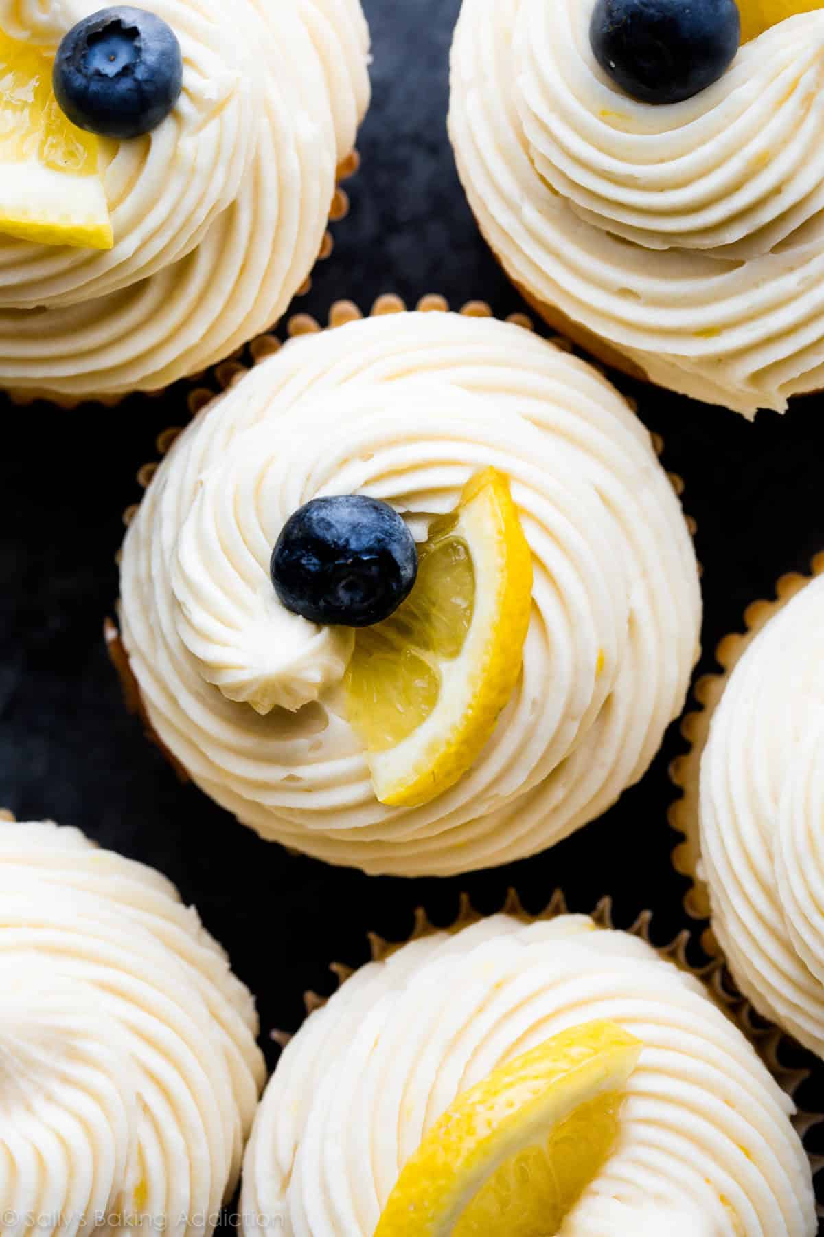 overhead image of lemon buttercream frosting piped onto cupcakes and topped with lemon slices and blueberries