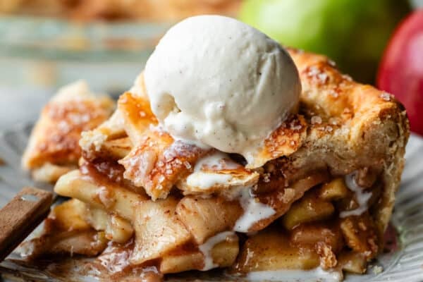 apple pie slice on plate with melty vanilla ice cream scoop on top.