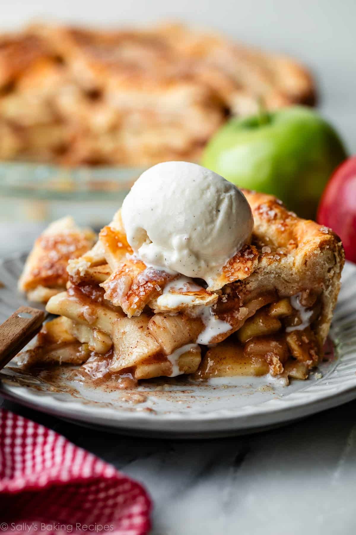 apple pie slice on plate with melty vanilla ice cream scoop on top.