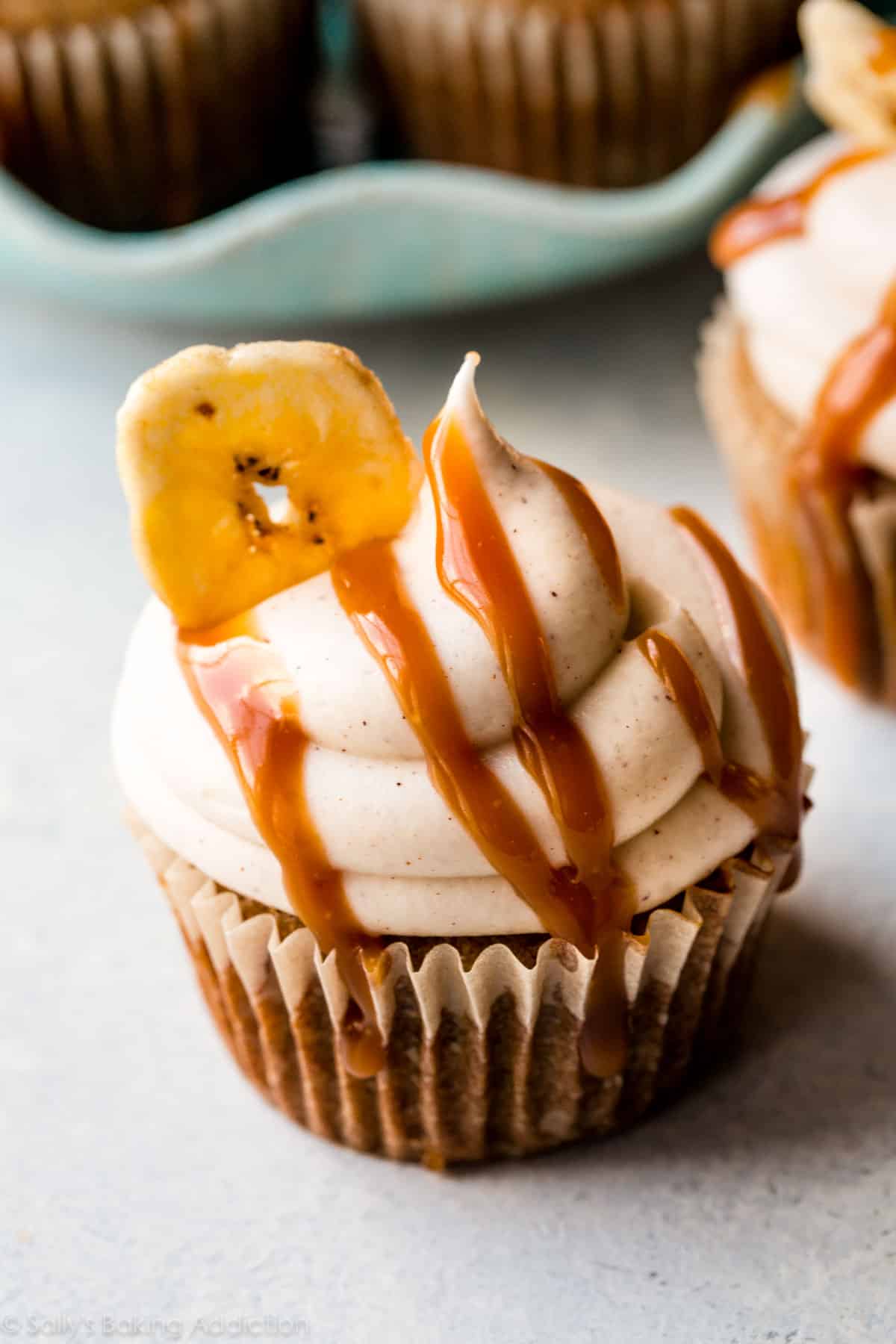 banana cupcake topped with cinnamon cream cheese frosting, salted caramel, and a banana chip