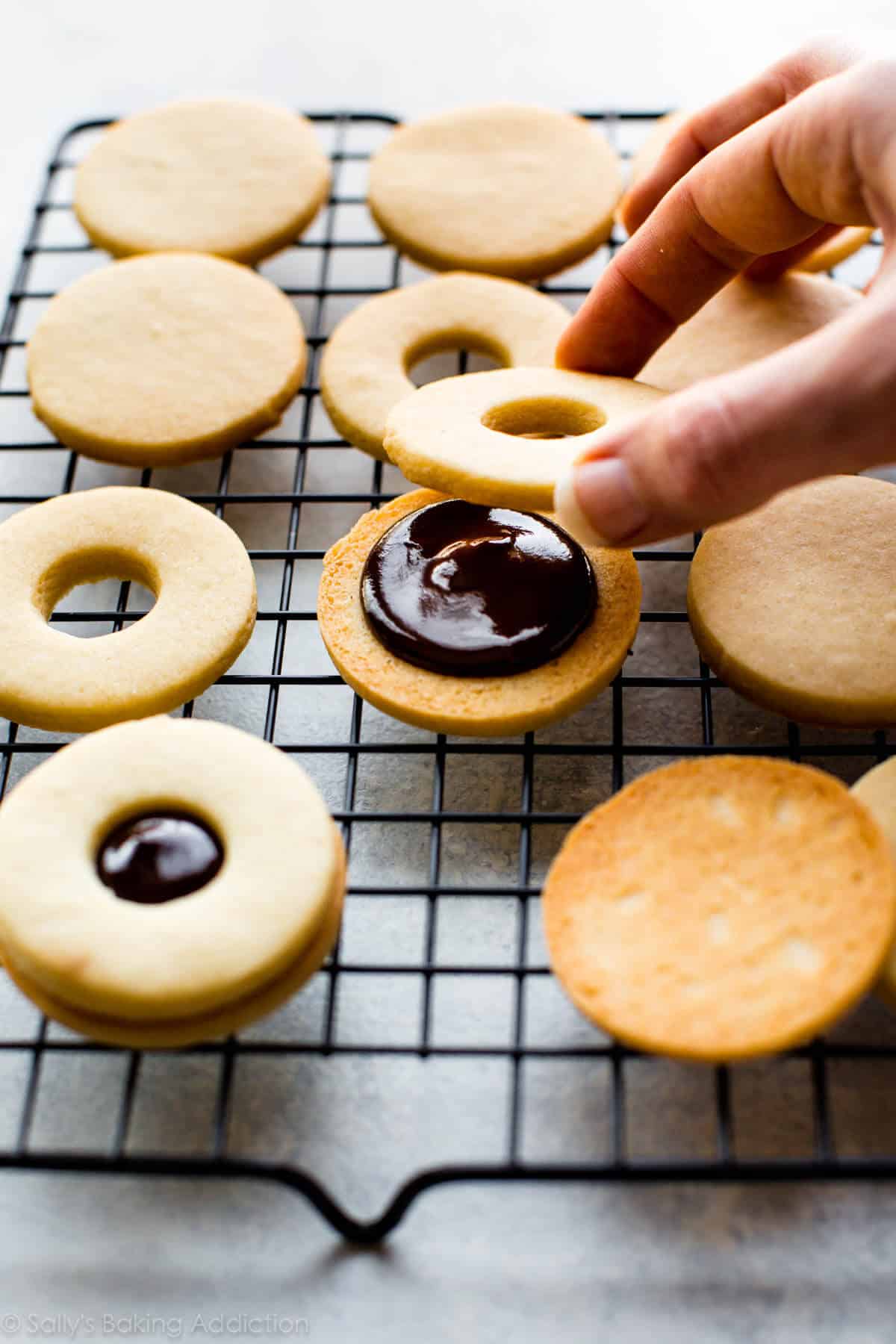 hands placing the top cookie onto the bottom cookie with chocolate ganache