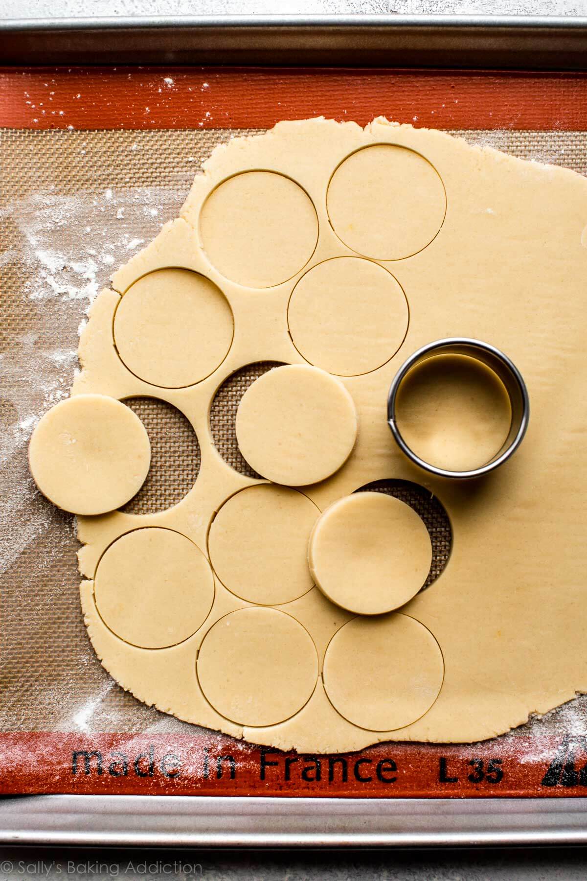 cookie dough rolled out onto a silpat baking mat on a baking sheet with a circle cookie cutter and circles cut out