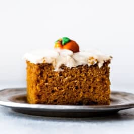 slice of pumpkin cake with cream cheese frosting on a silver plate