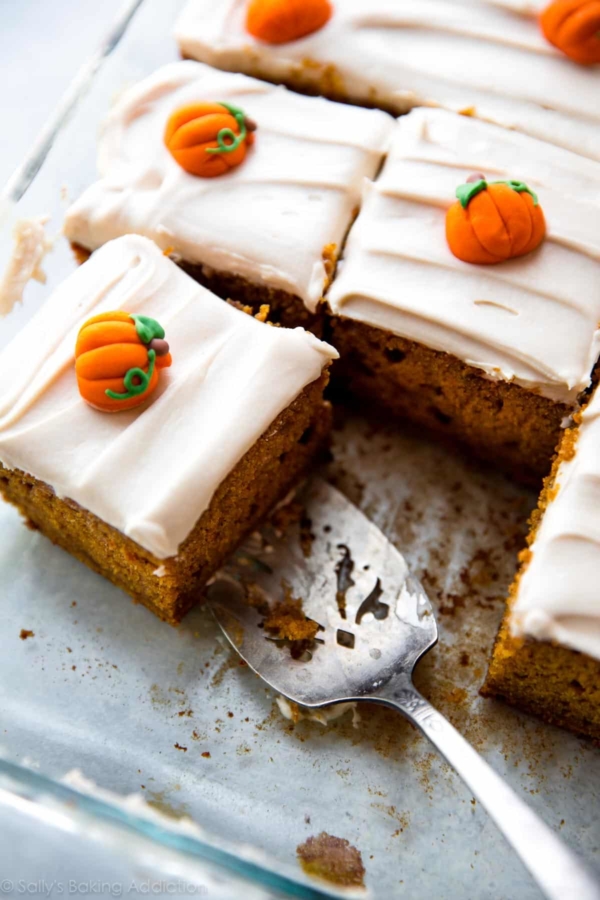 pumpkin sheet cake with cream cheese frosting in a glass baking dish cut into squares with a serving utensil