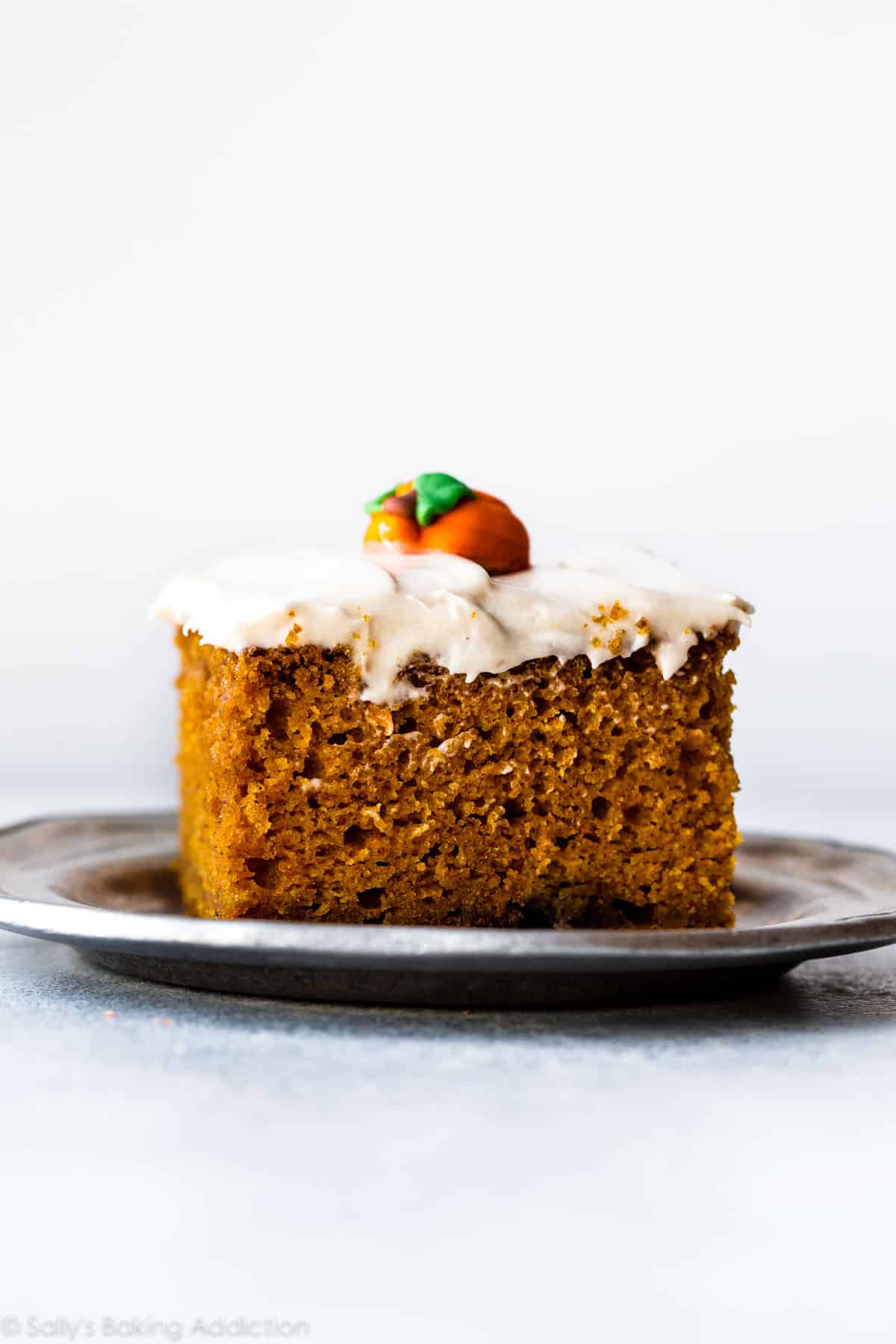 slice of pumpkin cake with cream cheese frosting on a silver plate