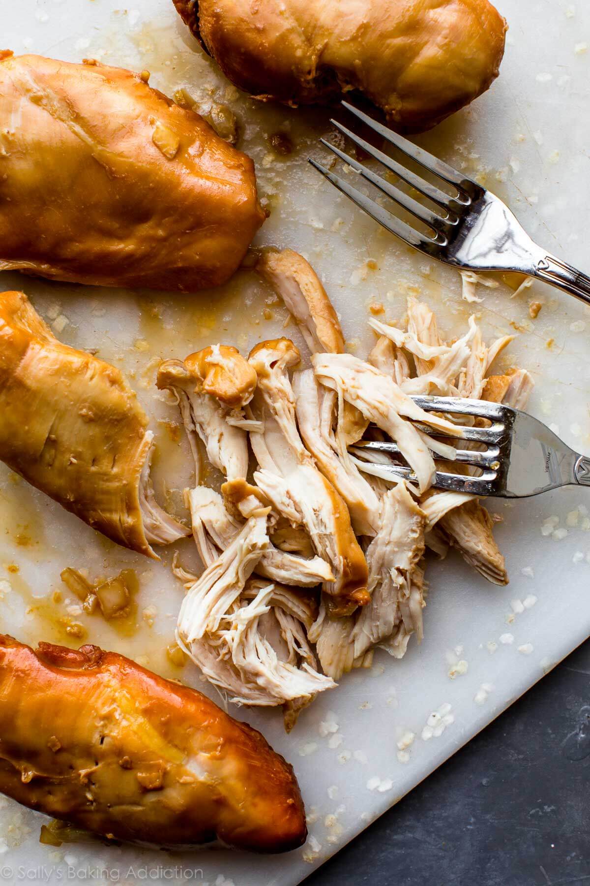 shredded chicken on a white cutting board with 2 forks