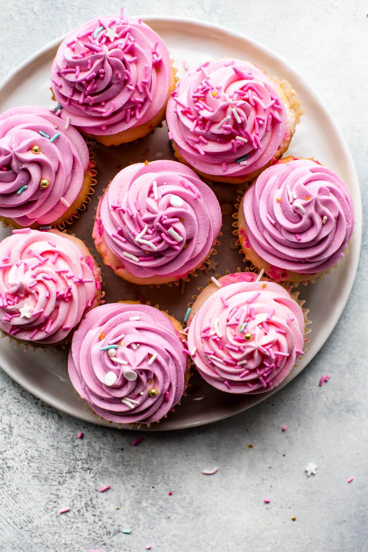 overhead image of cupcakes with pink buttercream frosting and sprinkles on a white plate