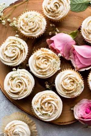 overhead image of vanilla wedding cupcakes with champagne frosting and gold sprinkles on wood server