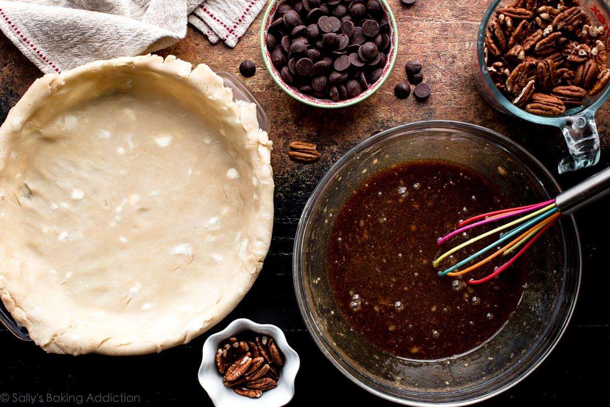 overhead image of pie dough in glass pie dish and ingredients in bowls for dark chocolate pecan pie