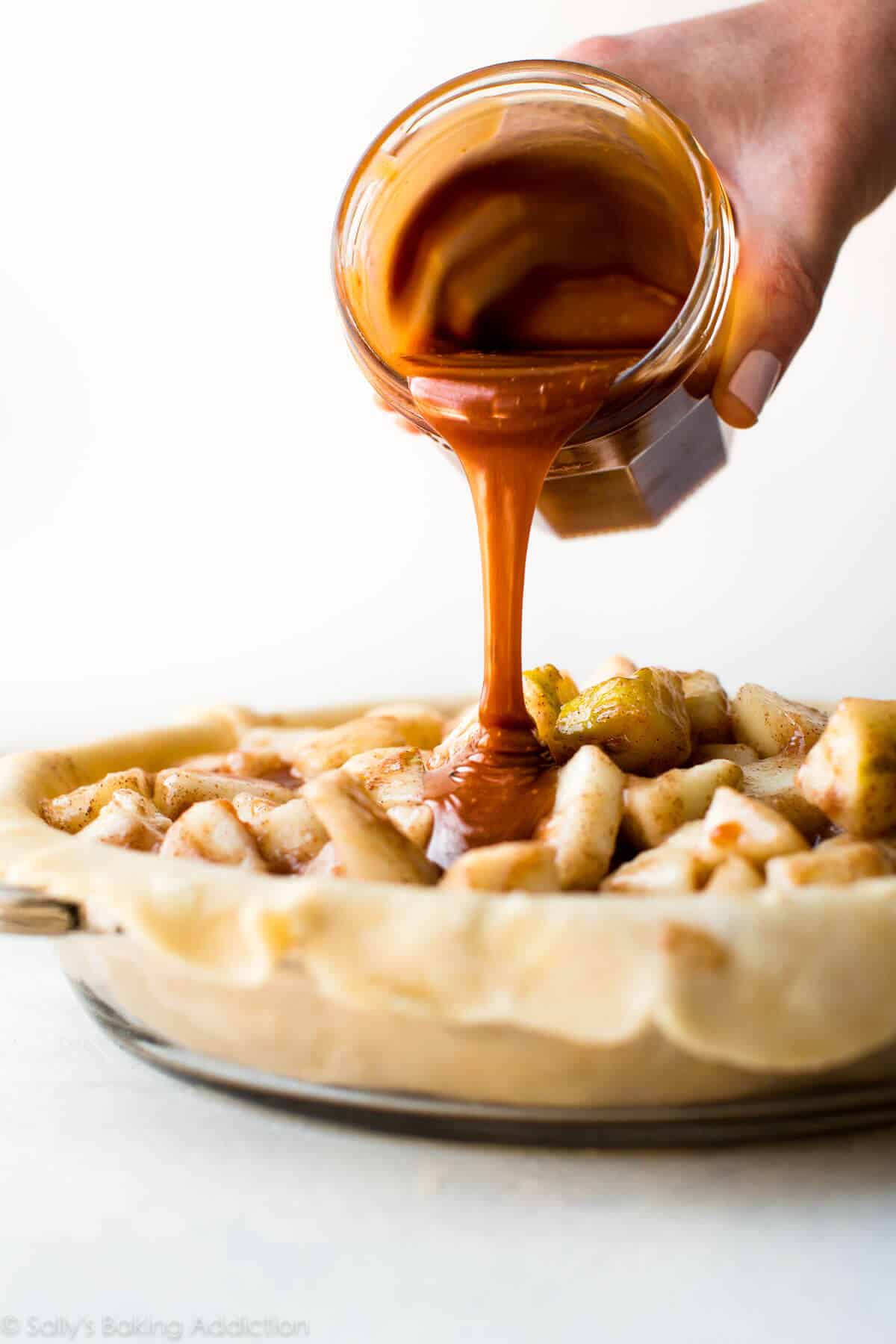 pouring salted caramel sauce onto pear pie filling before baking