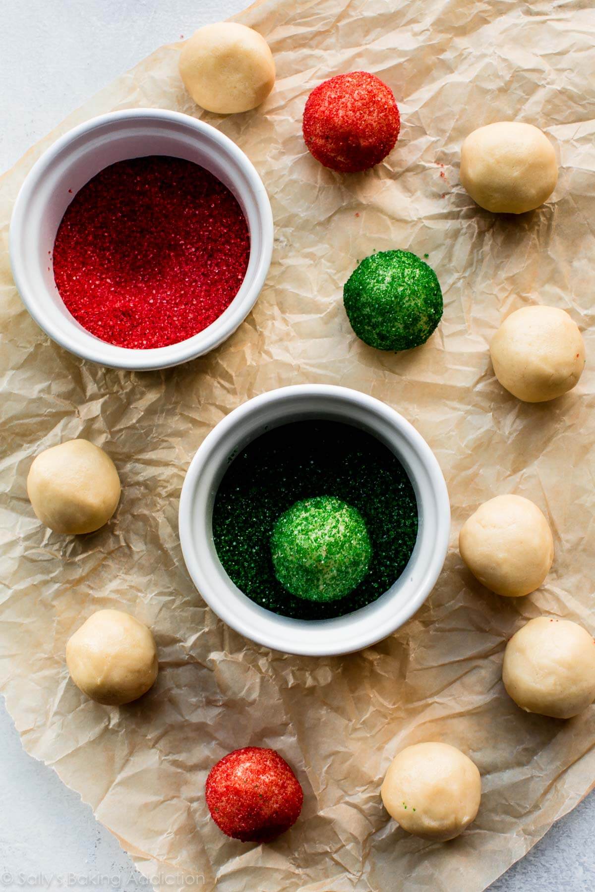 drop sugar cookie dough balls with bowls of red and green sprinkles