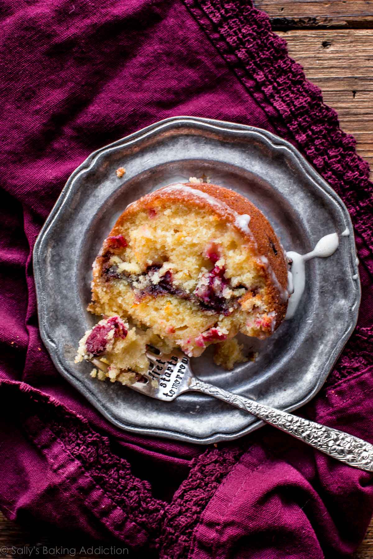 overhead image of a slice of cranberry orange bundt cake on a silver plate with a fork