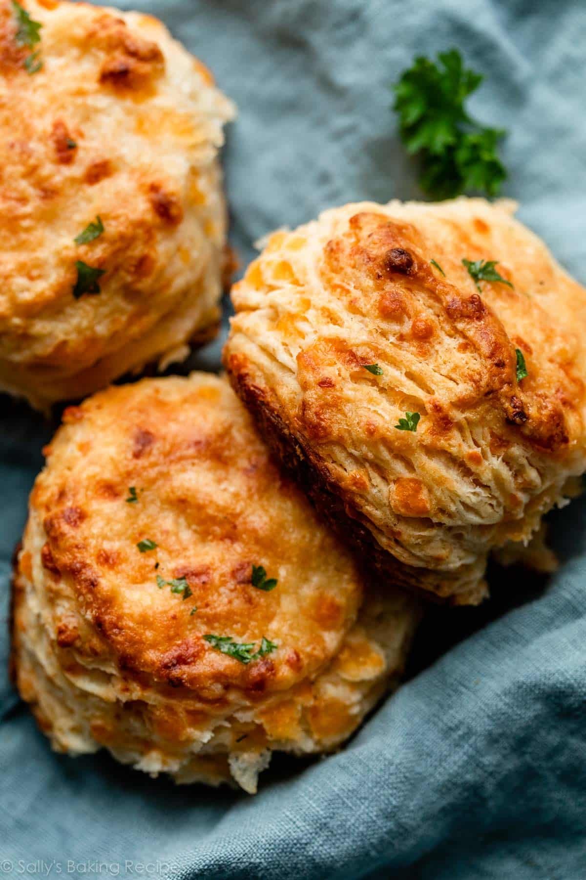 flaky cheddar biscuits on blue linen with fresh parsley sprinkled on top.