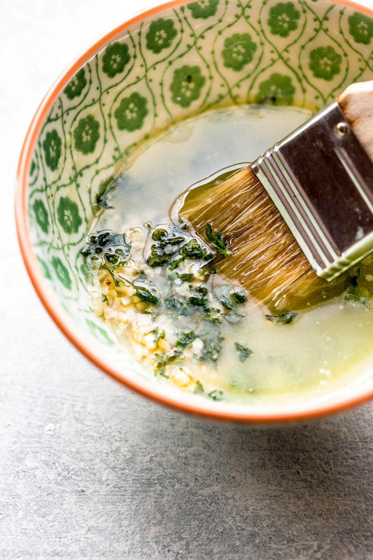melted butter with garlic and herbs in a bowl with a pastry brush