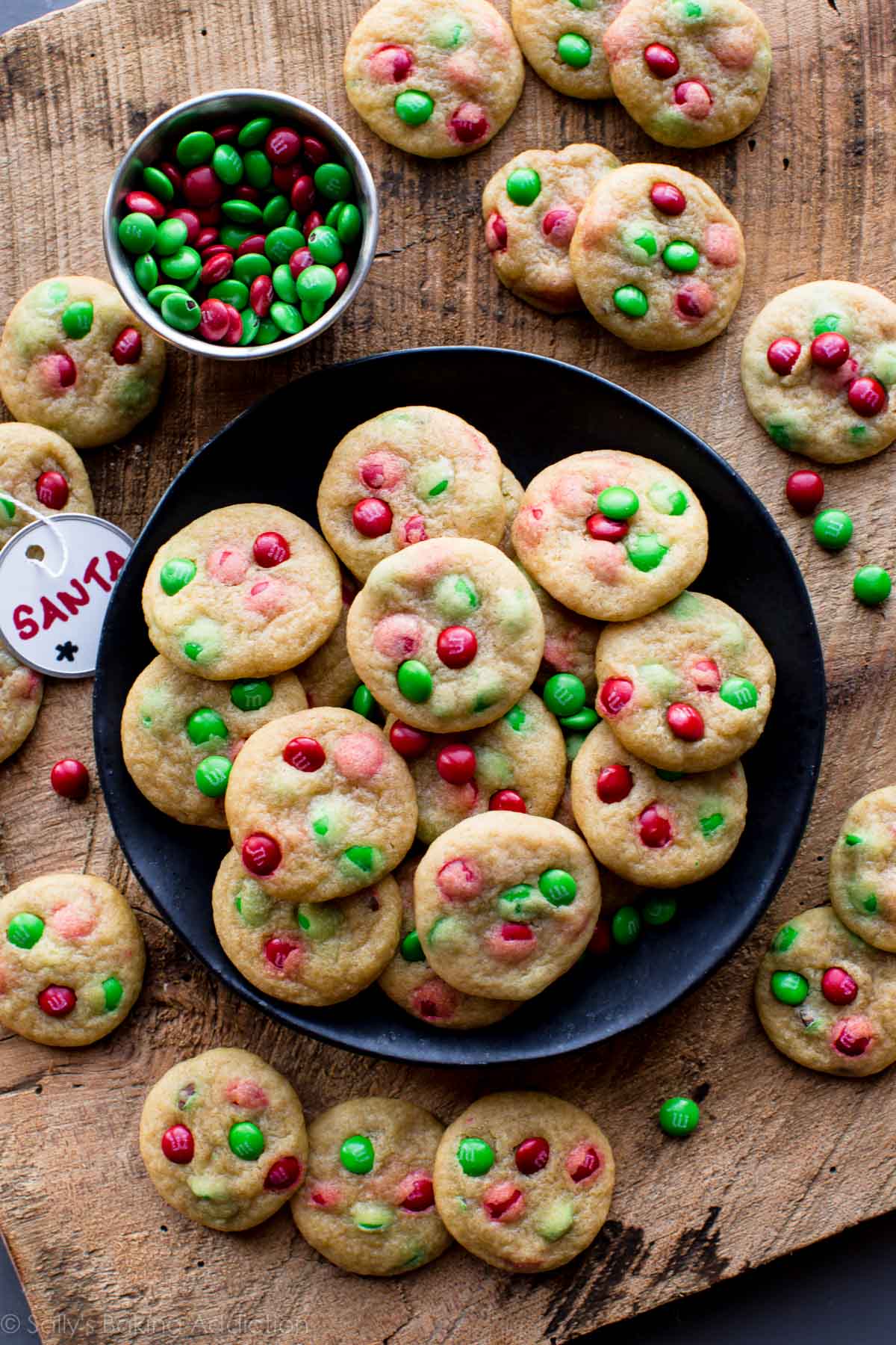 mini M&M cookies with Christmas M&Ms on a black plate with a Santa tag