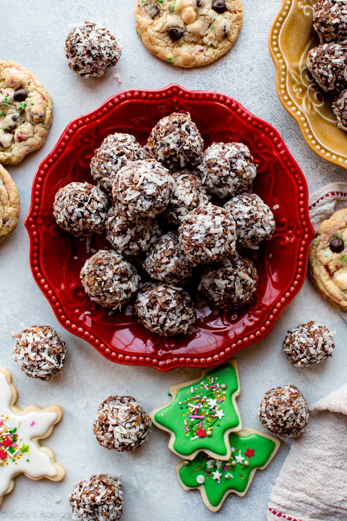 overhead image of no-bake chocolate coconut snowballs on a red plate with various other types of Christmas cookies