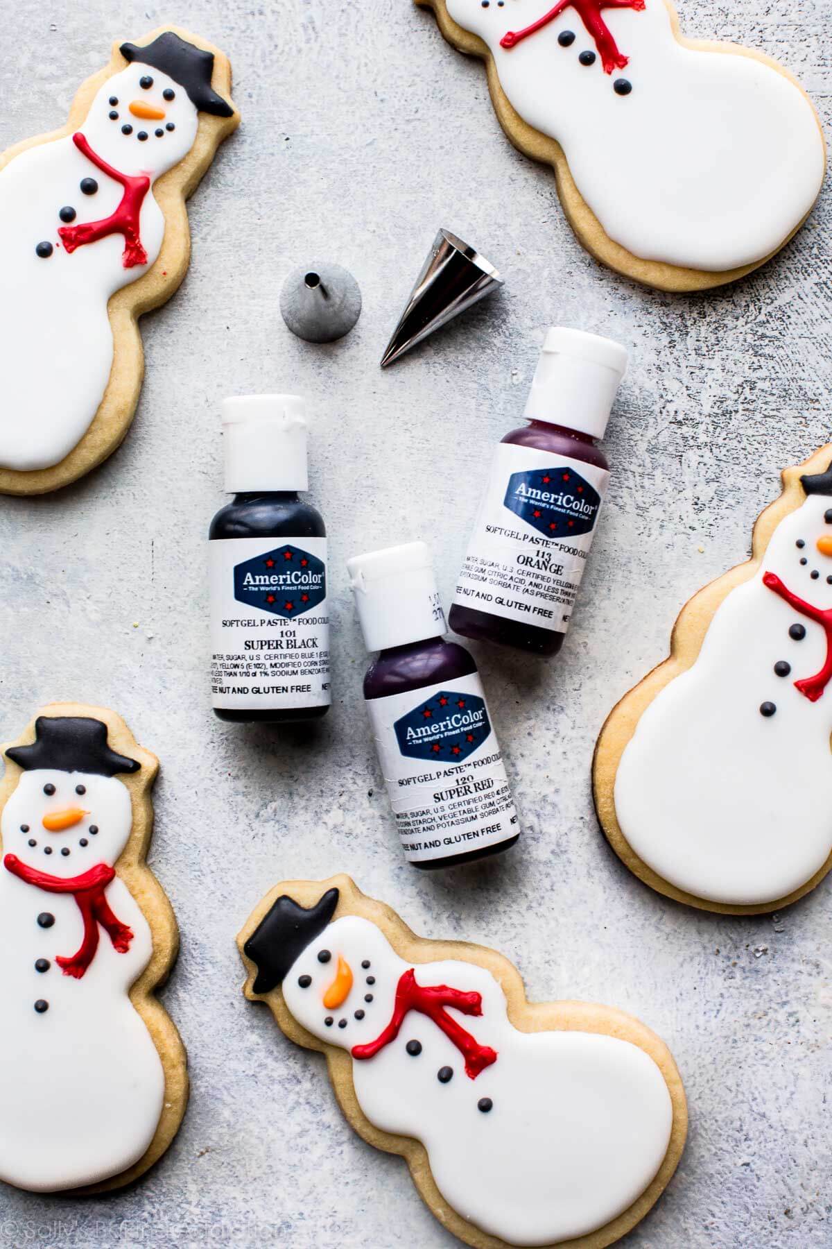 gel food coloring bottles, piping tips, and decorated snowman sugar cookies