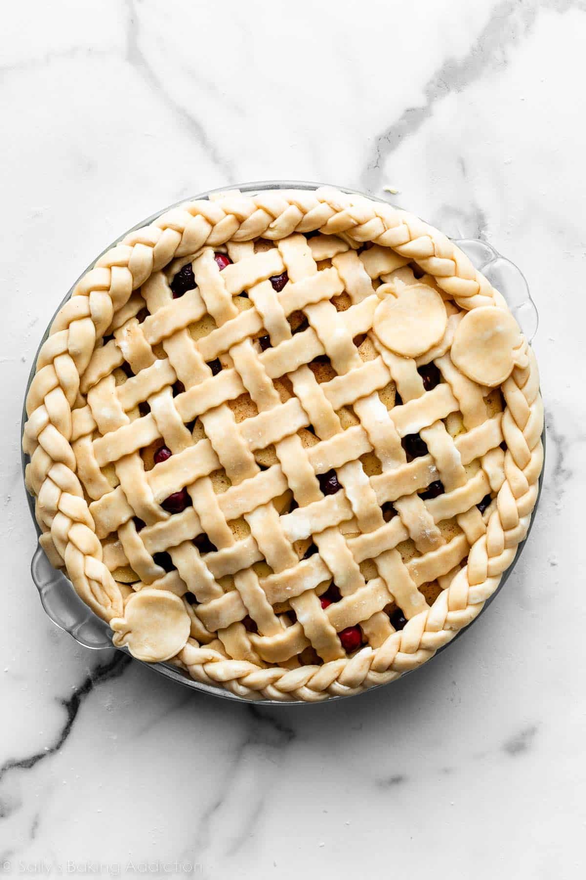 unbaked pie with wavy lattice pie dough, braided pie dough edge, and three apple pie dough shapes on top.