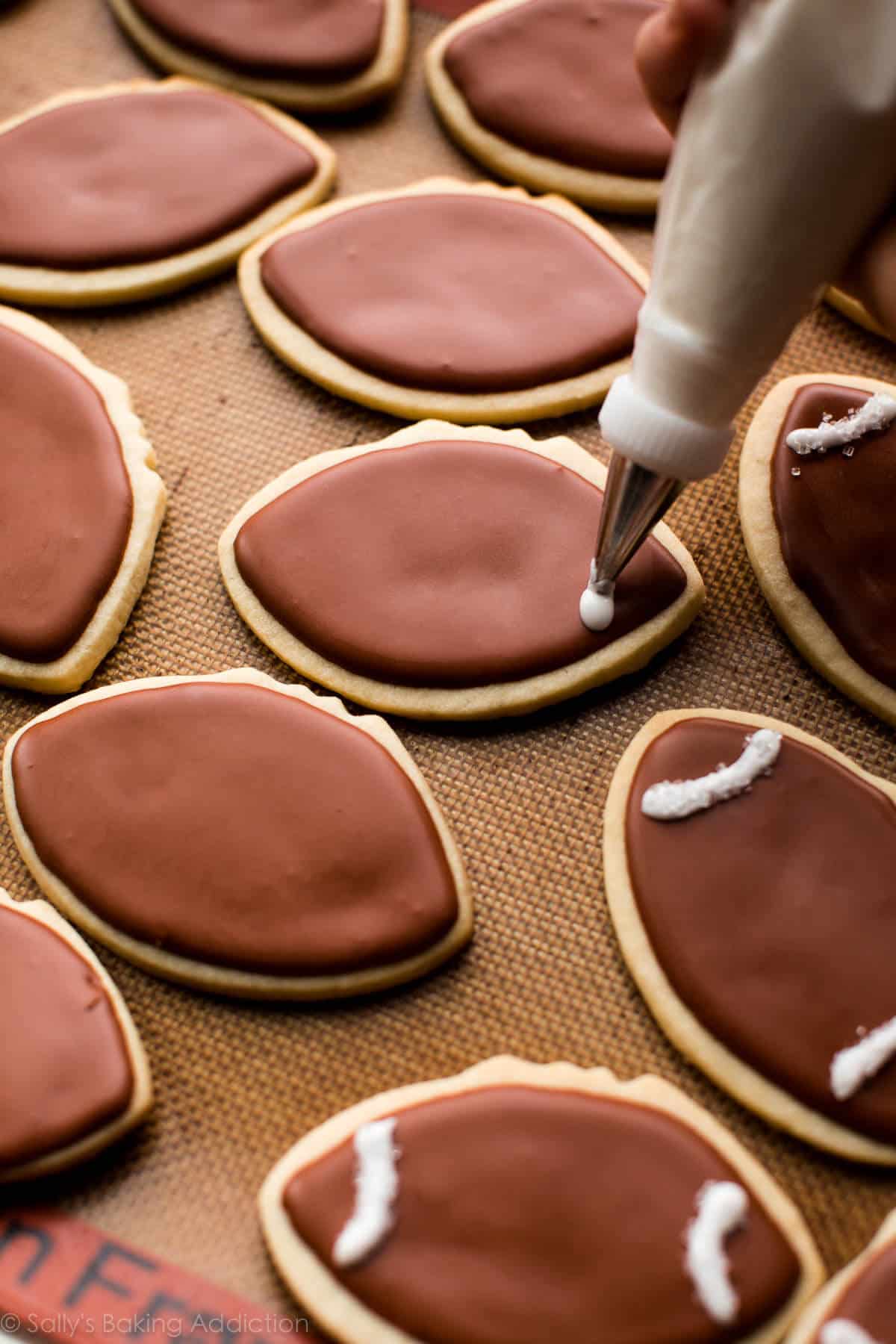 piping white details onto football sugar cookies