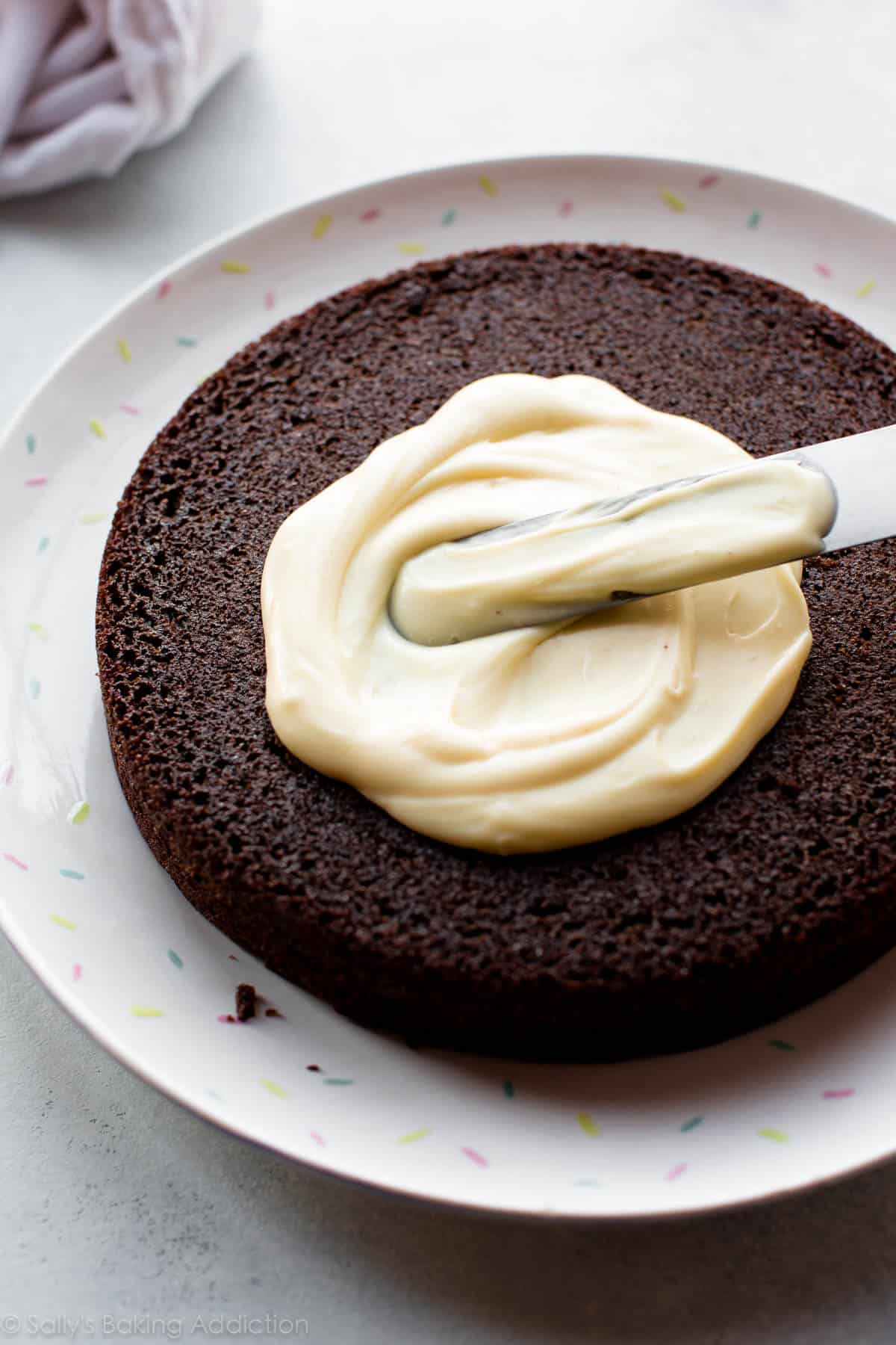 spreading white chocolate ganache on top of chocolate cake layer