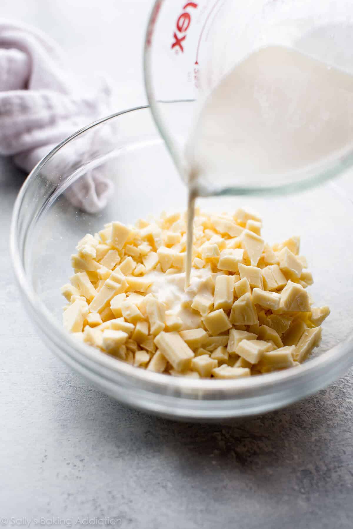 pouring heavy cream on top of white chocolate chunks in a glass bowl