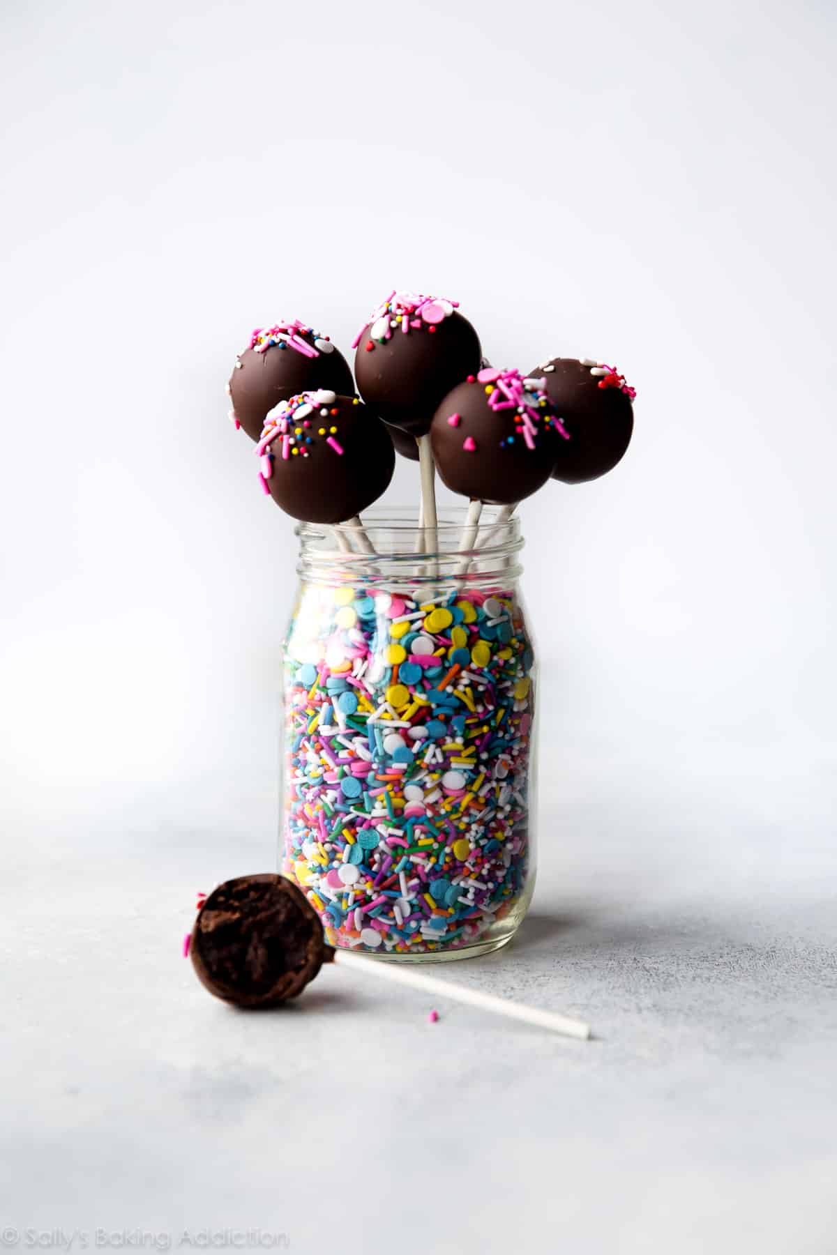chocolate cake pops standing up in a glass jar full of sprinkles