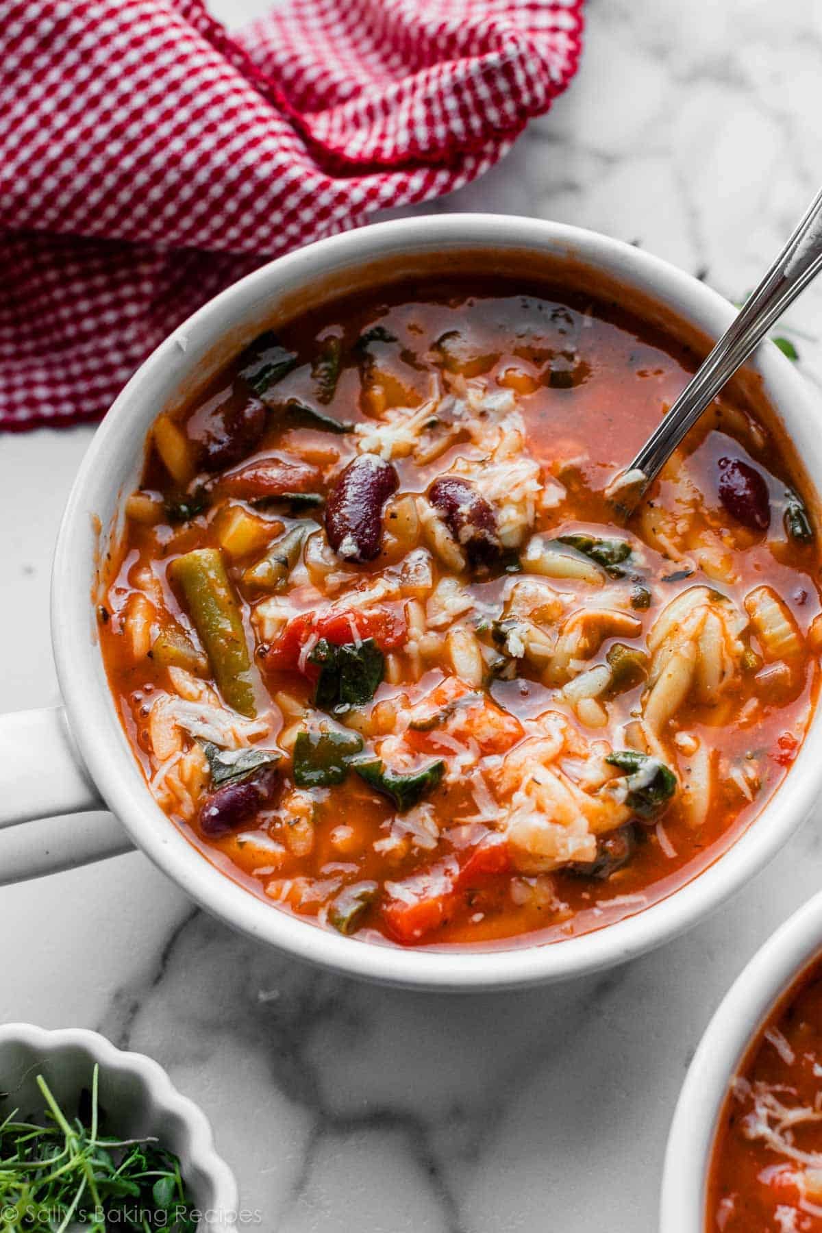 bowl of broth-based minestrone soup with beans and a spoon in it.