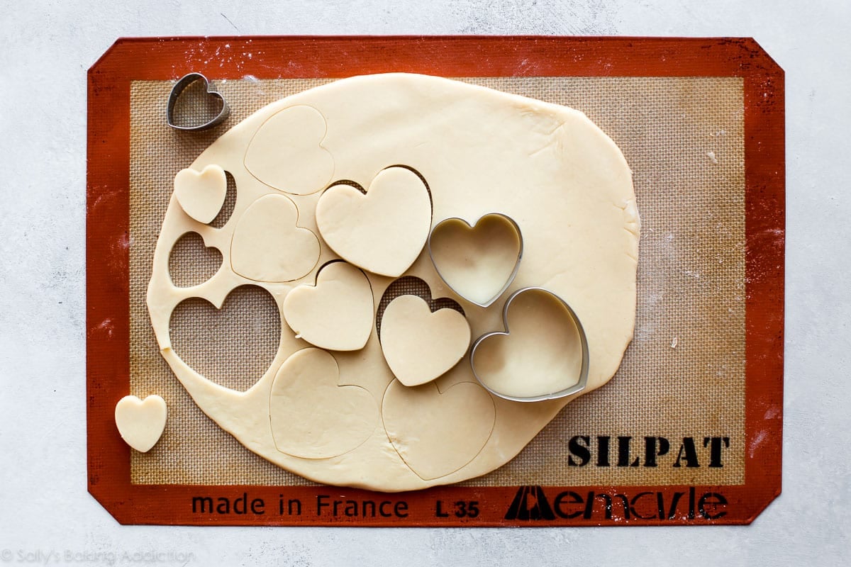 cutting heart cookie shapes with a cookie cutter from rolled out sugar cookie dough