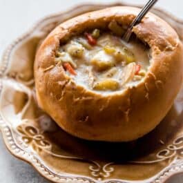 Chicken noodle soup in a bread bowl on a tan plate
