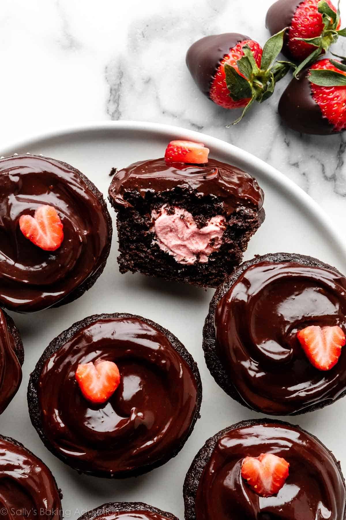 overhead image of chocolate covered strawberry cupcakes on a white plate with one sliced open.