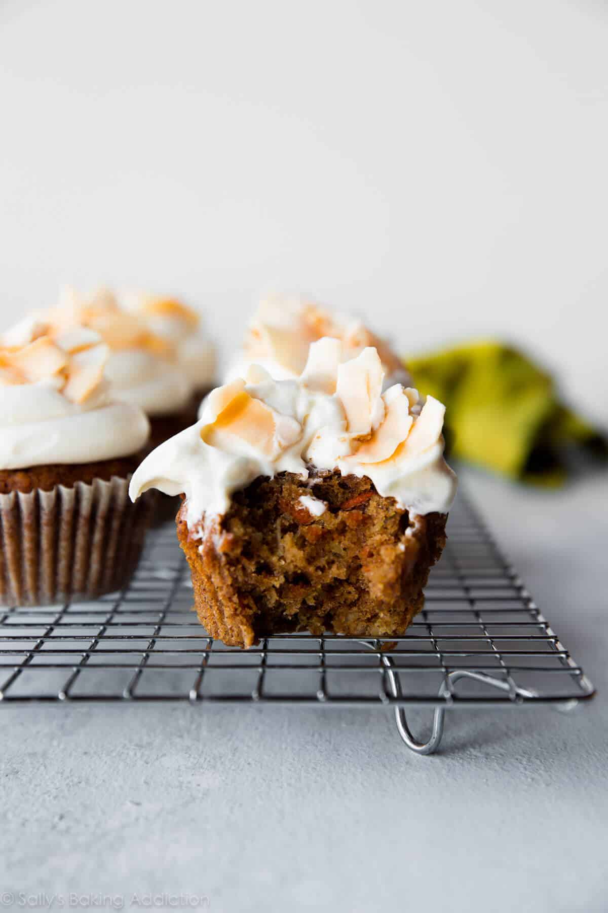 carrot cake cupcake with cream cheese frosting and toasted coconut flakes on a cooling rack