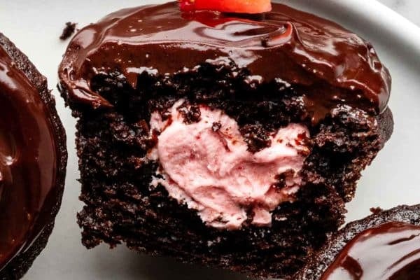 close-up of chocolate covered strawberry cupcake filled with strawberry buttercream and sliced open.