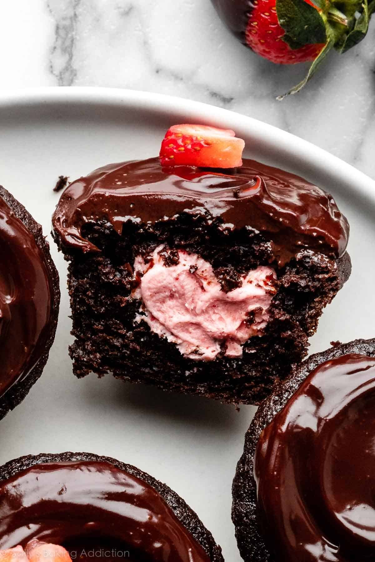 närbild av choklad täckt jordgubbscupcake fylld med jordgubbssmörkräm och skivad öppen.