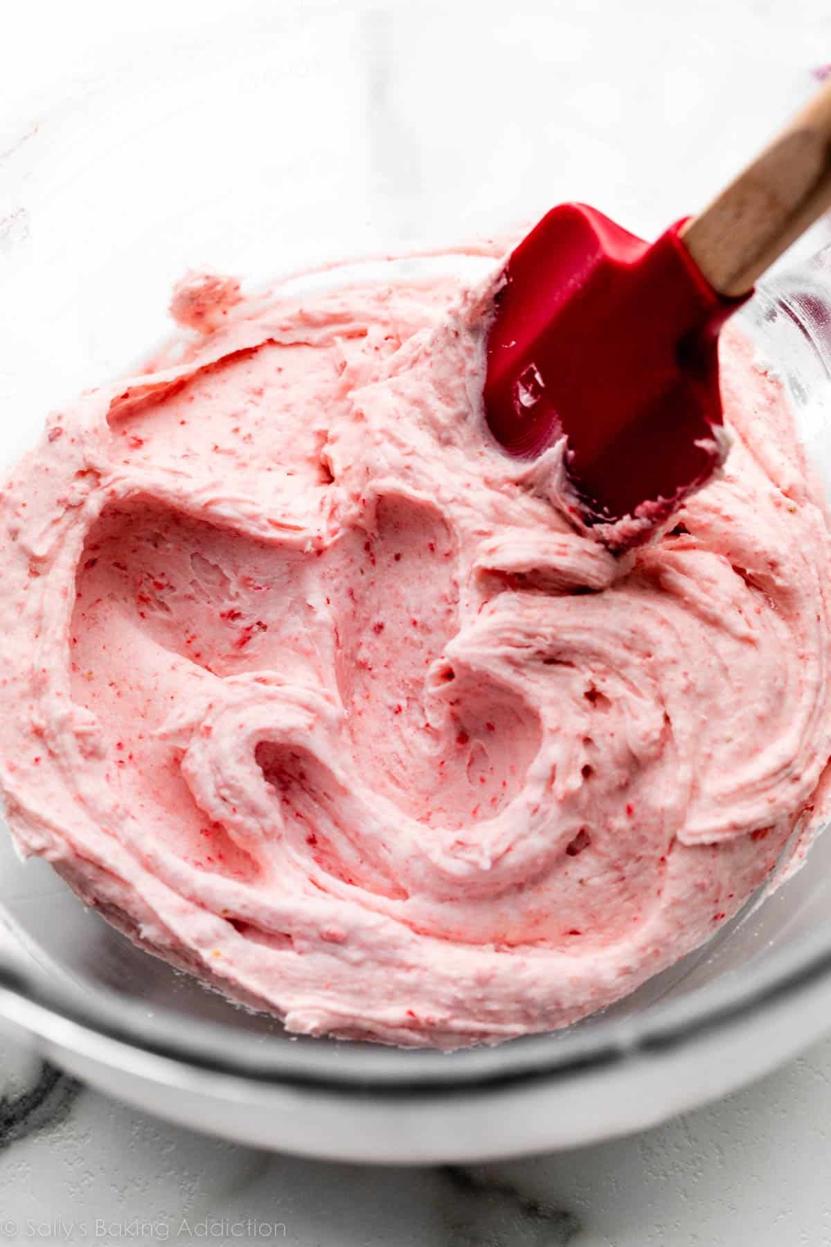 strawberry buttercream filling in glass bowl with red spatula.