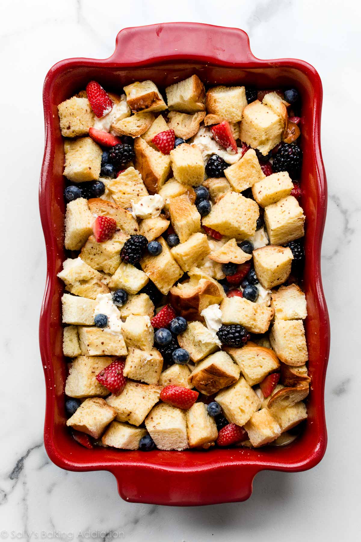 cubed challah bread, berries, and cream cheese mixture layered in red casserole dish