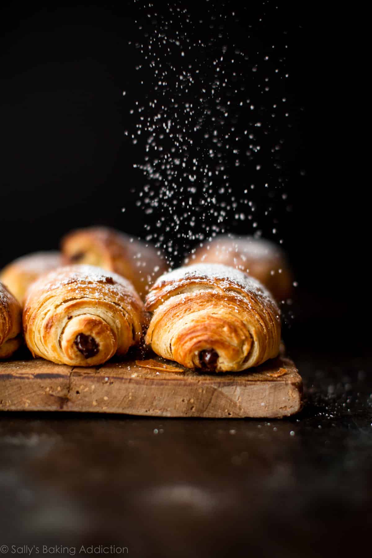 chocolate croissants on a wood serving tray with confectioners' sugar