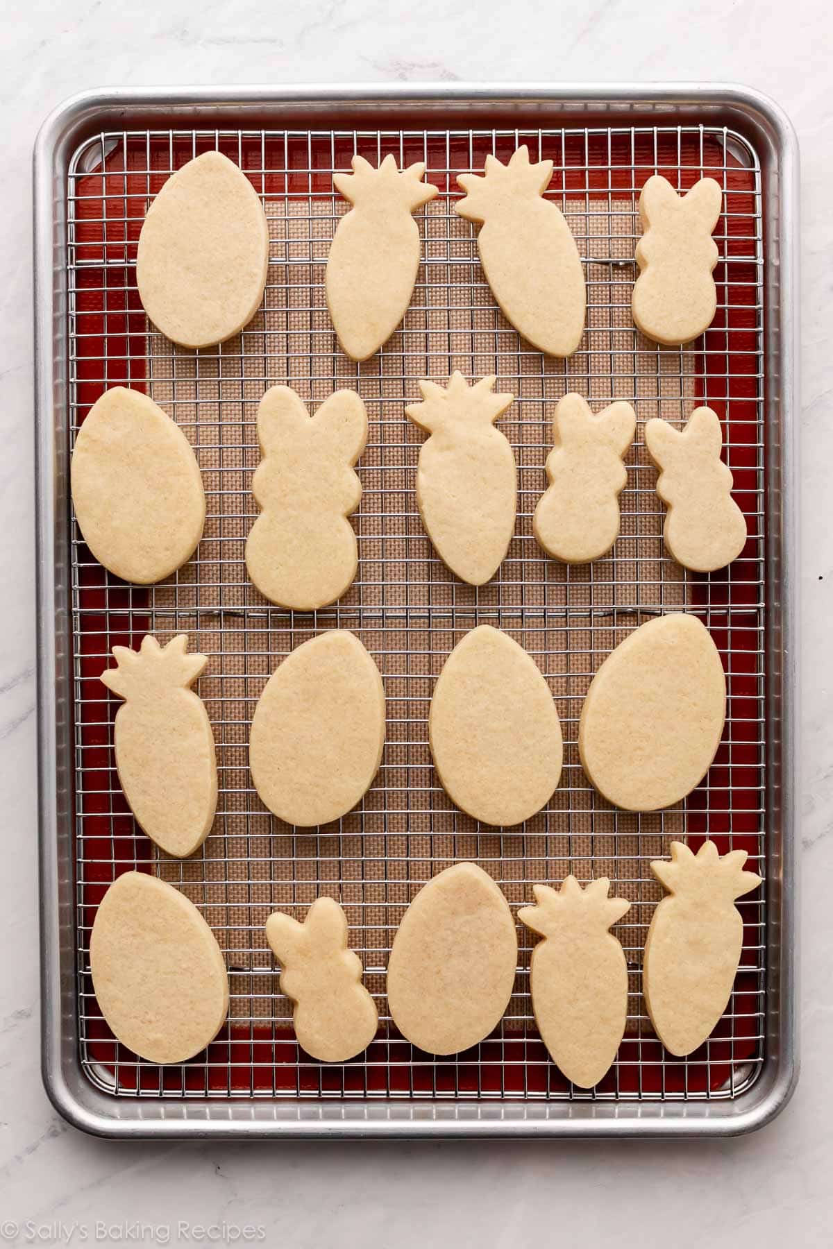 bunny, carrot, and egg shaped cookies on cooling rack on top of baking sheet.