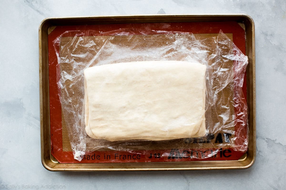 croissant dough rolled into a rectangle on a baking sheet with plastic wrap