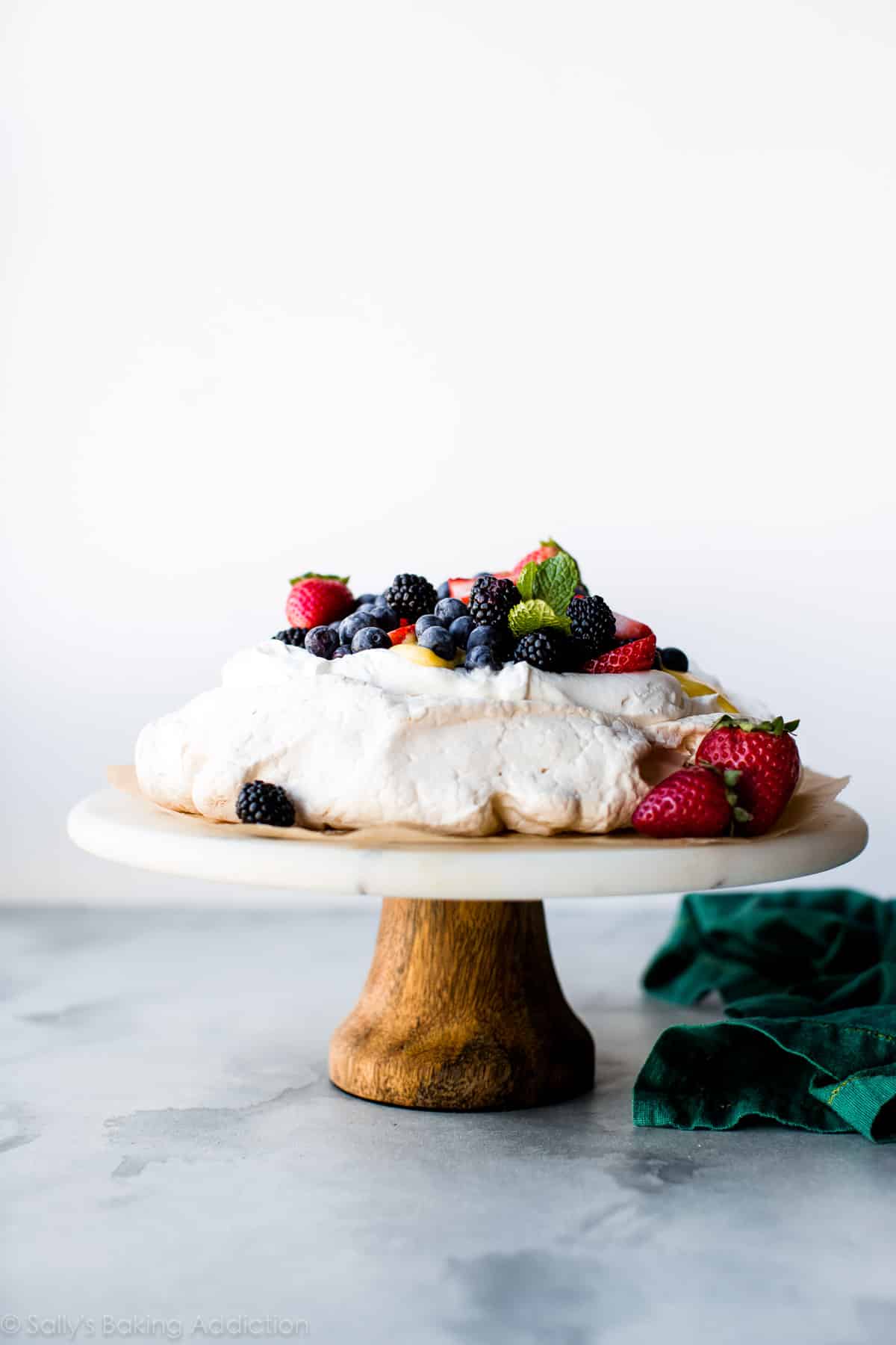 pavlova with fresh fruit topping on a marble and wood cake stand