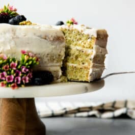 pistachio cake on a wood and marble cake stand with a slice on a cake server