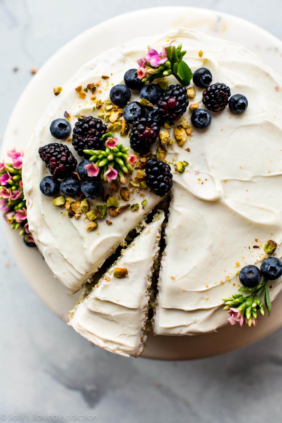 overhead image of pistachio cake with cream cheese frosting and berries and pistachio garnish