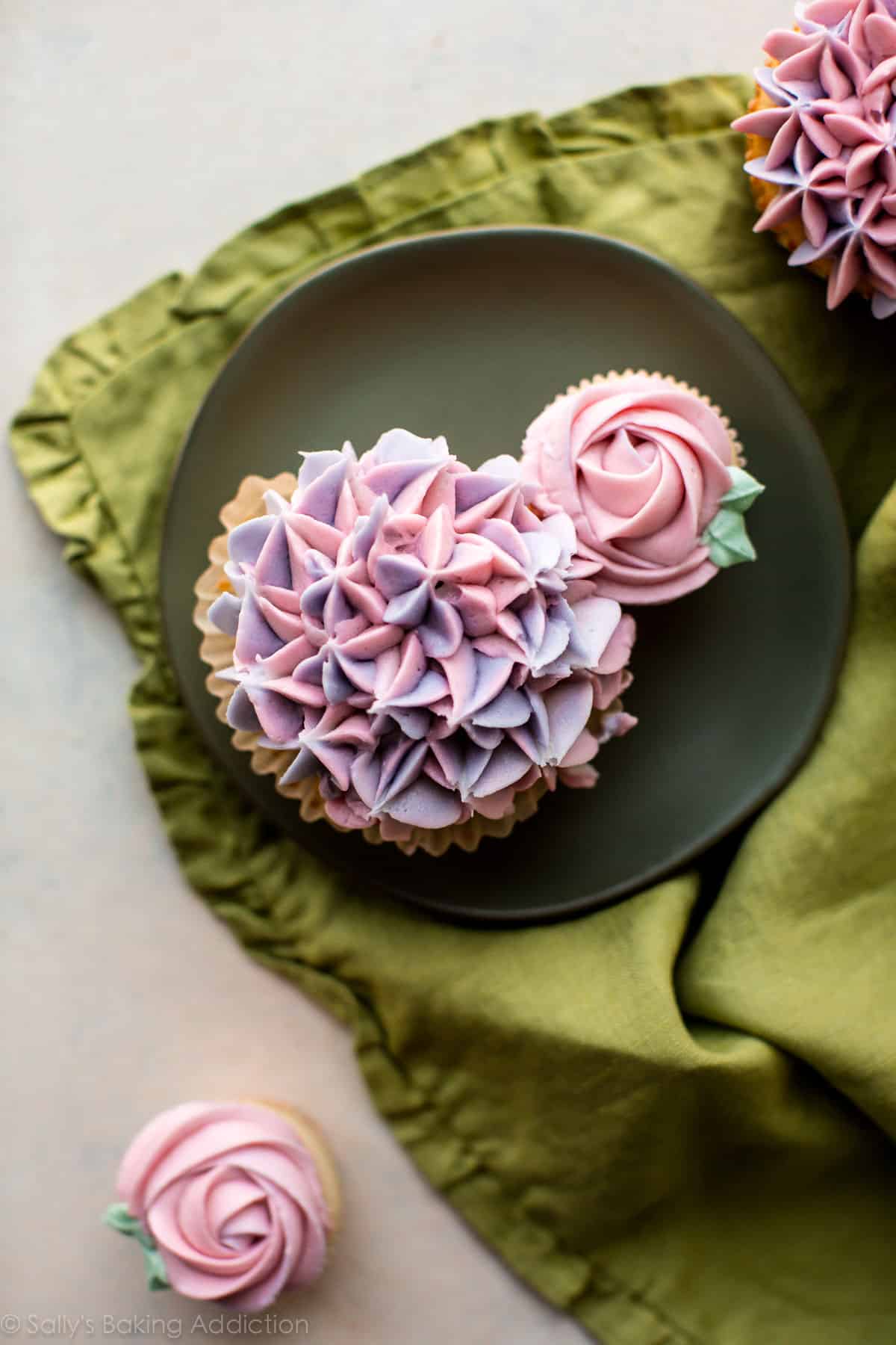 cupcakes decorated with buttercream like hydrangea and roses on a green plate
