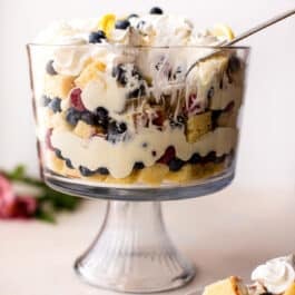 lemon berry trifle with a serving spoon and a serving of trifle on a white plate