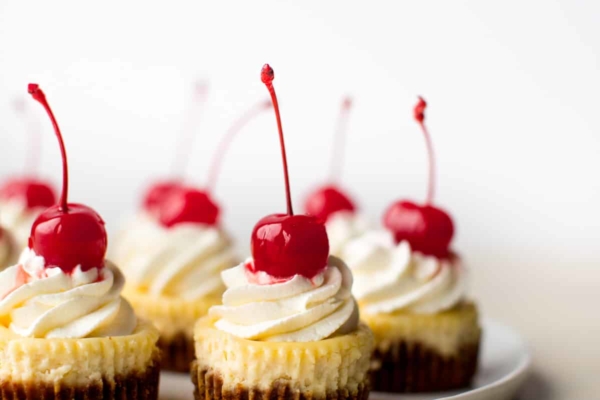 mini cheesecakes with whipped cream and cherries on top on a white plate