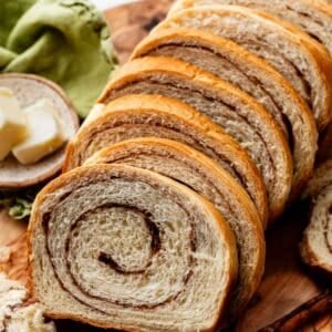 slices of homemade cinnamon swirl yeasted bread on wooden serving board with green linen in background.
