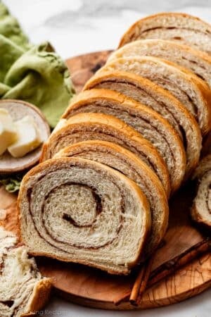 slices of homemade cinnamon swirl yeasted bread on wooden serving board with green linen in background.